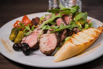 Roasted meat with blood in a cut with vegetables on a wooden background