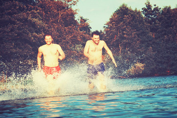 Glückliche junge Menschen laufen und springen am See beim Sonnenuntergang