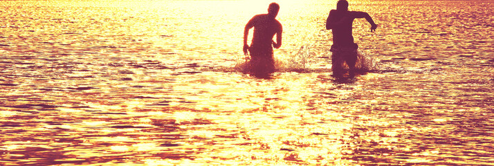 Glückliche junge Menschen laufen und springen am See beim Sonnenuntergang