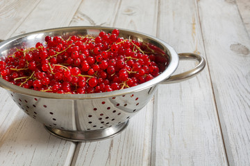 Colander full of freshly harvested red currants on wooden background. Side view. Summer.
