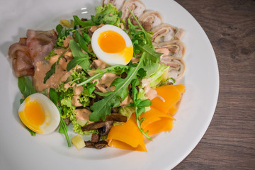 Salad with egg and mushrooms on a white plate and a wooden background