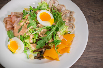 Salad with egg and mushrooms on a white plate and a wooden background