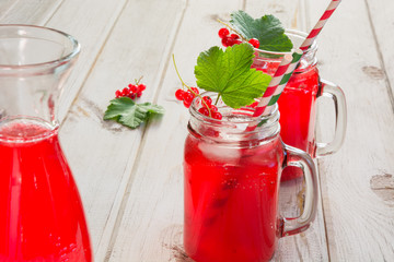 Homemade red currant lemonade in a mason jar and garnish of berry branch on ligth wooden table.