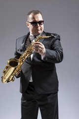 Fototapeta premium Caucasian Saxophone Player in Sunglasses Posing with Saxophone in Studio Environment.