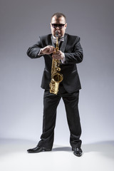 Music and Musicians Ideas and Concepts. Full Length Portrait of Caucasian Mature Saxophone Player in Sunglasses Playing the Instrument Against White.