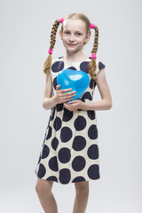 Portrait of Funny Caucasian Blond Girl With Pigtails Posing in Polka Dot Dress Against White. Holding Blue Air Balloon.