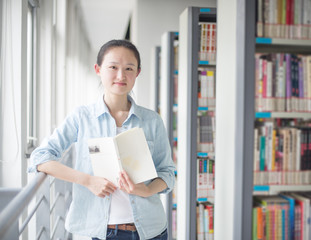 Portrait of a smiling young student reading a book in a library