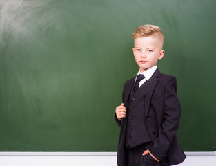 Boy in a suit standing near empty green chalkboard