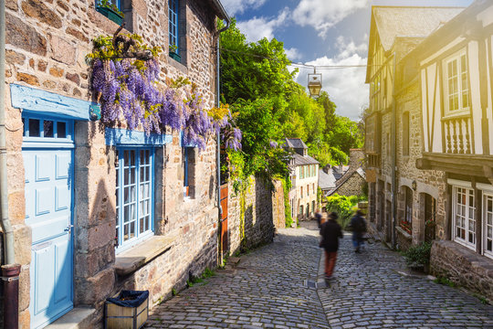 Beautiful view of scenic narrow alley with historic traditional houses and cobbled street in an old town of Dinan with blue sky and clouds. Brittany (Bretagne), France