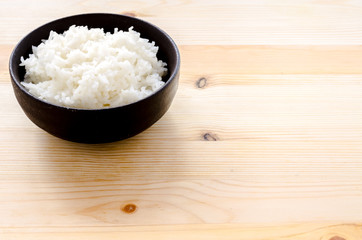 Rice in the black bowl on wood table background