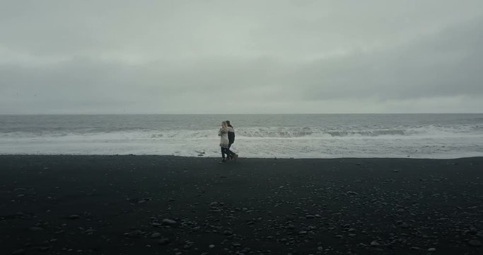 Aerial view of young couple walking on black volcanic beach. Man and woman have a date on shore of the sea in Iceland.