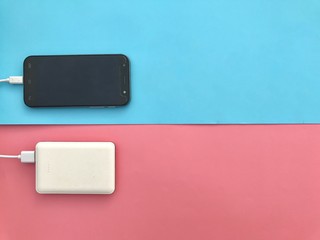  Closeup A black smartphone charging with A white powerbank set on light blue and pink background.Gadgets on colorful background.Top view with Copy space.Selective focus.