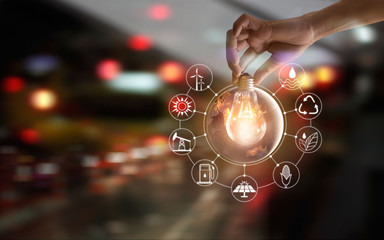 Hand holding light bulb in front of global show the world's consumtion with icons energy sources