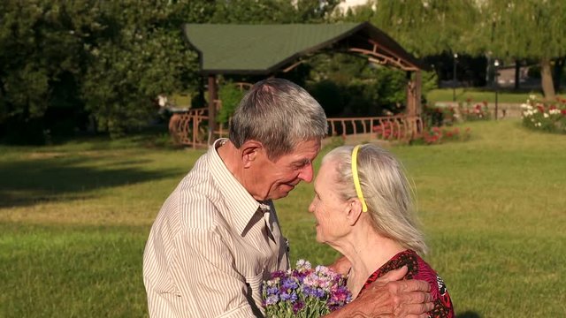 Touching family couple of eighty years are stand in an embrace in the park against the backdrop of grass.