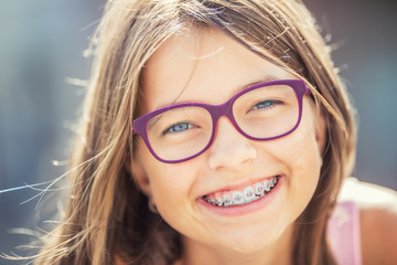 Happy smiling girl with dental braces and glasses. Young cute caucasian blond girl wearing teeth...