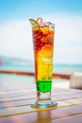 Close up of glass with refreshing layered cocktail with lime on table on beach.