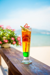 Close up of glass with refreshing layered cocktail with lime on beach.
