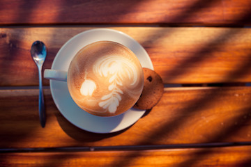 A cup of coffee with pattern in a white cup with cookie on wooden background