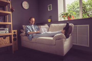 Modern home office concept. Freelancer lying on sofa working with laptop. Toned image.