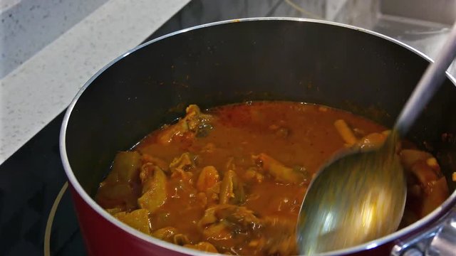 Cooking curry chicken being stirring with spoon.