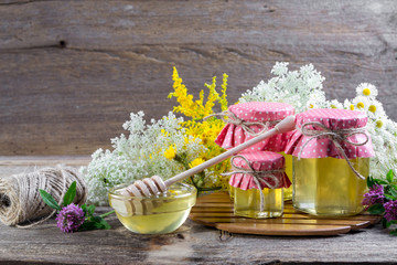 Full fresh liquid honey pots and honey stick with summer wild flowers on rustic wooden table,...