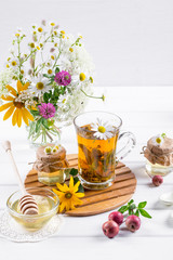 Herbal tea with herbs and flowers in a glass tea pot with honey. Bouquet of flowers on white table