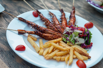 Potato fries with fry prawns, lettuce salad. Isolated over wooden background