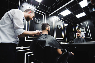 Fototapeta na wymiar Master cuts hair and beard of men in the barbershop, hairdresser makes hairstyle for a young man