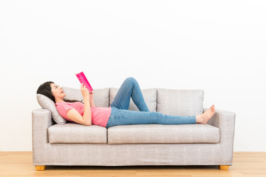 woman reading book in living room lying on couch