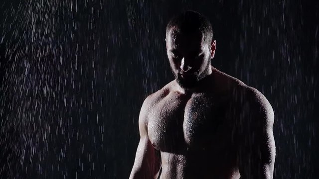 close-up. a man with a large muscular body. beautiful male Breasts. face with a beard. the room is dark and from the ceiling water flows. rough male skin dripping