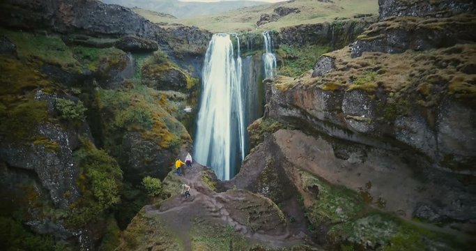 Aerial view of the tourists exploring the territory of Gljufrabui waterfall in Iceland. Copter moves away from people.