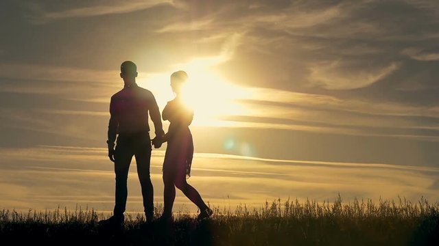 Silhouette of a young couple walking toward the sunset. The concept of love.