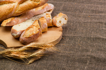 still life with French fresh bread baguettes with poolish on a wooden cutting board and wheat....