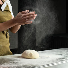 woman baker sprinkled flour on roll dough on a wooden board. Process of preparing pizza. Cooking time, cooking concept, selective focus