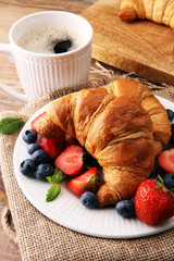 Delicious breakfast with fresh croissants, coffee and ripe berries on old wooden background