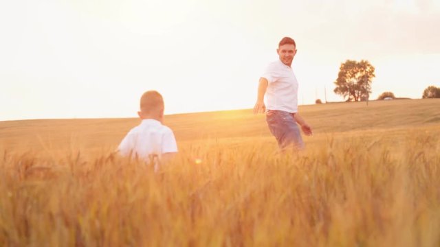 Father calls his son. Happy father and little son walking in summer field and having fun.