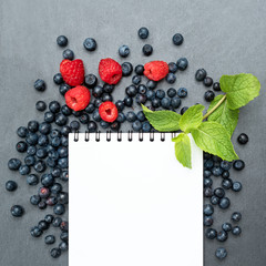 Blueberries, raspberries, mint and notepad for writing notes or resolutions, concept of diet, slimming, detox, healthy lifestyles and nutrition. Mock up, space for text.