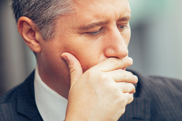 Face of pensive mature businessman covering mouth