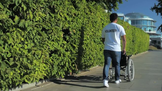 Rear view of a merciful volunteer pushing a wheelchair