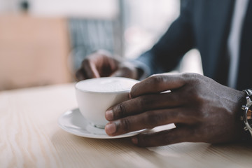 cropped view of african american businessman holding coffee cup in cafe