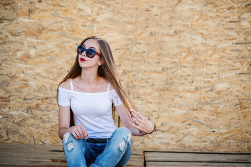 Portrait of a beautiful girl sitting on wooden boards against veneer wall.