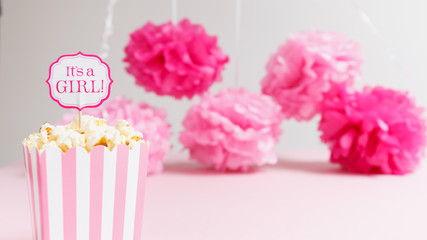 It's a girl sign in a popcorn bag at the baby shower party.  Paper flowers background.  Baby shower celebration concept