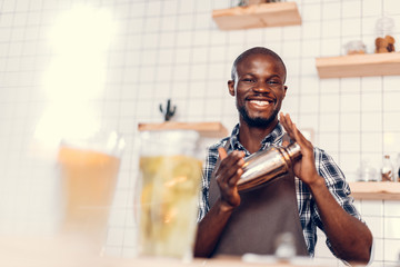 smiling handsome african american bartender making cocktail in shaker on bar counter