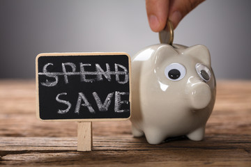 Hand Putting Coin In Piggybank By Spend Save Sign