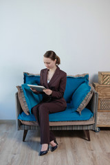 Smiling businesswoman working on digital tablet in a bright office isolated on a brick wall background. Looking directly at the camera. Girl in elegant office suit.