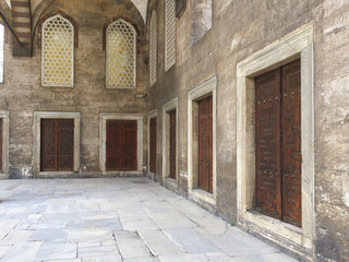Portico with doors in a row and grids in the courtyard of an ancient mosque