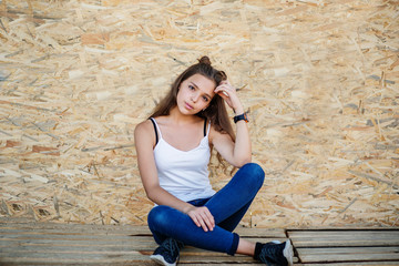 Portrait of a beautiful girl sitting on wooden boards against veneer wall.