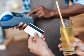 cropped view of person paying with credit card, waiter with terminal standing behind in cafe