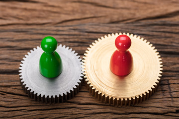 Red And Green Pawn Figurines On Interlocked Cogwheels