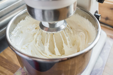 Closeup of electric mixer with whipped smooth dough for cake. Batter being whipped. Mixing white dough in bowl with motor mixer, baking cake